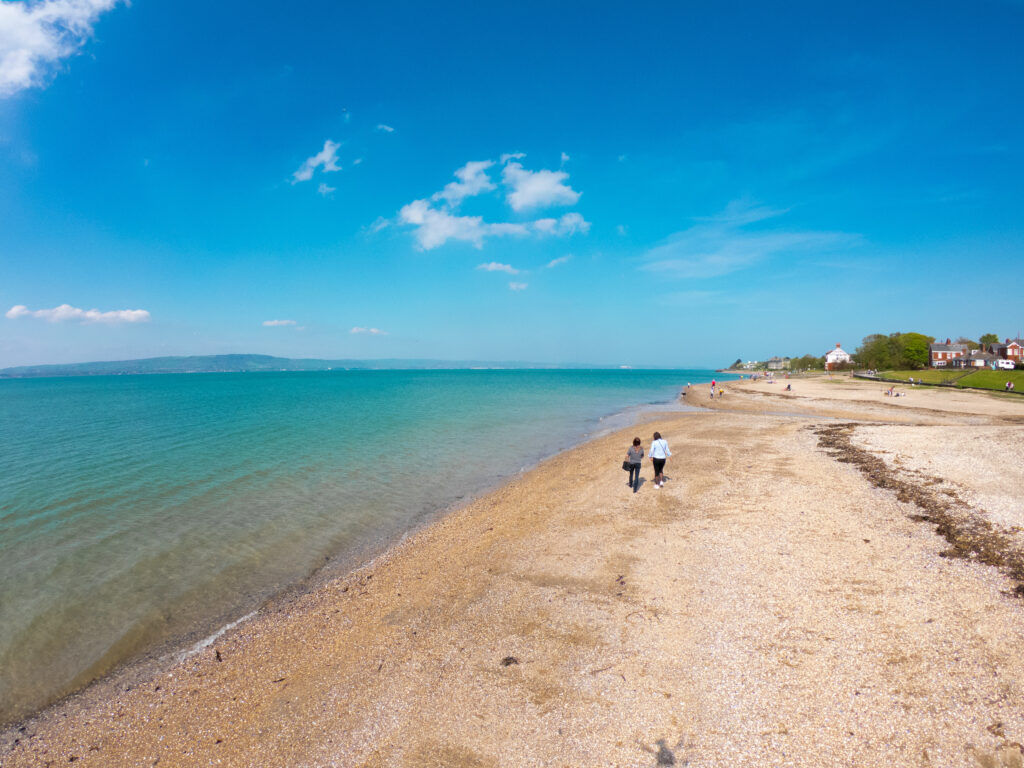 Back view of two women standing on beach and looks at sea against blue sky in Holywood, Northern Ireland, aerial view